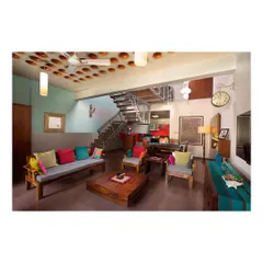 Another view of the Interlocking House living area, highlighting the solid teak wood furniture. The simple, strong forms of the sofa and chairs provide a durable and timeless foundation for the room's eclectic decor.