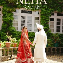 A bride in a stunning red lehenga leads her groom, dressed in elegant white, through the ivy-covered courtyard of a heritage palace. This classic wedding portrait captures the timeless grace and grandeur of the wedding day.