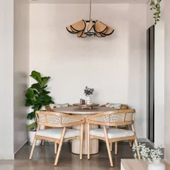 This cozy dining nook features a round wooden table and chairs with woven rattan backs, creating a warm and inviting atmosphere. The statement pendant light adds a touch of modern, sculptural art to the space.