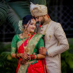 A stunning portrait of a traditionally dressed Maharashtrian couple. The bride's green and red saree and gold jewelry are perfectly complemented by the groom's elegant attire.