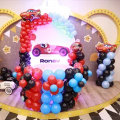 A "Cars" themed birthday party setup. This features a race track-inspired cake table with red, black, and blue balloons and cutouts of Lightning McQueen.