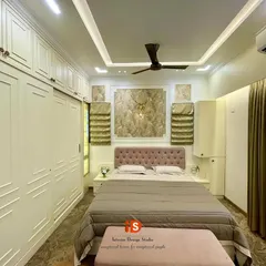 A master bedroom designed with a classy English look. The room features white Duco-finished wardrobes with classic molding, a soft pink tufted headboard, and elegant Roman blinds, all contributing to a bright and sophisticated aesthetic.