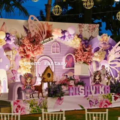 A magical fairy garden party for Nishvika, glowing under the evening sky. This enchanting setup includes a whimsical purple fairy house, large butterfly wing props, custom name lettering, and soft lighting from hanging lanterns to create a dreamlike atmosphere.
