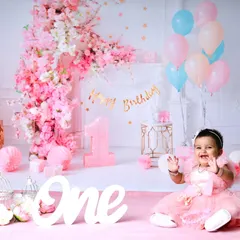 An adorable first birthday shoot with an elaborate pink floral arch and balloon display. This little girl's joyful expression makes the entire scene come alive.