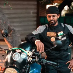 A classic rider portrait. This individual, leaning against his bike, exudes a calm confidence. The photo highlights his riding gear and the patches that signify his belonging to the biker community.