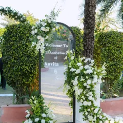 A classic and elegant welcome to a 25th-anniversary party. A mirrored sign is framed by an arch of delicate white flowers, setting a pure and romantic tone.