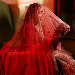A dramatic bridal portrait with a red veil. The lighting creates a moody and romantic feel, highlighting the richness of her attire.