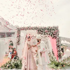 A shower of petals rains down as the couple exchanges garlands. This is a classic Varmala shot, capturing the peak of the ceremony's joy and celebration.