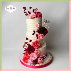This elegant three-tiered cake features a rustic textured buttercream and a stunning cascade of sugar flowers in shades of deep red and soft pink. The subtle ombre effect on the bottom tier adds a touch of modern sophistication.
