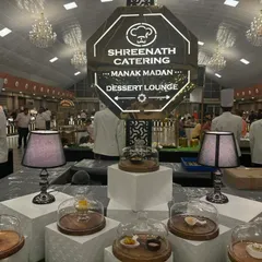 This is a view of one of my full-scale Dessert Lounge setups for a large wedding. The custom-lit octagonal sign and elegant displays with glass cloches create a sophisticated and inviting atmosphere for guests to gather.