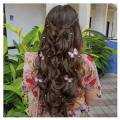 A dreamy Mehendi hairstyle with a fishtail braid and soft waves. The look is decorated with small pearls and butterfly clips for a playful, magical feel.