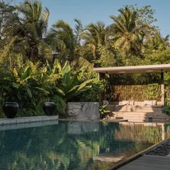 A view of the pool with the gazebo in the background. The design focuses on clean lines and natural materials, allowing the dense greenery to be the main feature of this tranquil outdoor space.