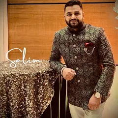 A client wearing a premium Jodhpuri suit made from pure pashmina wool. The fabric has a beautiful woven paisley pattern, and the look is completed with a classic pocket square and brooch.