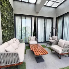 This balcony in Yojna Vihar was transformed into a chic outdoor lounge. The design features a vertical green wall, modern woven furniture, and patches of artificial turf for a comfortable and stylish retreat.