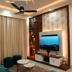 A cozy living room setup featuring a TV unit with vertical wooden slats and built-in-plant holders. The design is complemented by a false ceiling with spot lighting, creating a warm and inviting atmosphere.