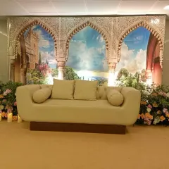 A themed stage backdrop featuring a print of scenic Moroccan arches. The setup is completed with a comfortable sofa and floral arrangements, transporting guests to another place.