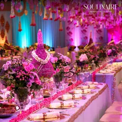 A breathtakingly long dining table set for a lavish wedding, adorned with dramatic pink floral arrangements and traditional motifs. Our tablescapes are designed to be the centerpiece of your celebration.