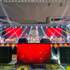 A head-on view of the concert-style stage we built. The setup includes large speaker stacks, a branded DJ booth, and a vibrant red LED backdrop, creating a professional and immersive experience.