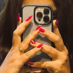 A classic and confident look. These sharp, stiletto-shaped nail extensions are painted in a vibrant red, with a single accent nail featuring delicate gold and rhinestone detailing.