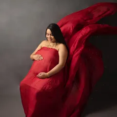 A dramatic solo portrait in a vibrant red gown. The flowing fabric creates a sense of movement and power, beautifully highlighting the baby bump.