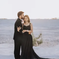 A tender moment in a stark, beautiful landscape. The groom's gentle kiss on the bride's forehead contrasts with the dramatic, sweeping train of her black gown.