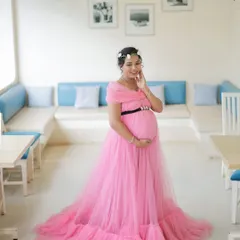 A solo portrait showcasing our popular off-shoulder pink maternity gown. The ruffled train and simple black belt create a chic and elegant look.