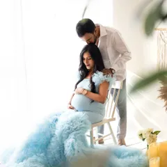 A tender moment between the expecting couple. The soft blue gown pools around her, surrounded by the warm glow of candles, creating a romantic and dreamy maternity portrait.