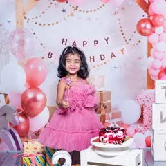 A little girl celebrating her second birthday with a big smile. The pink balloon arch, presents, and birthday cake create a perfect party scene for her special day.