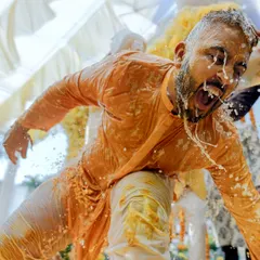 A dynamic, candid shot capturing the groom's reaction mid-splash during his Haldi ceremony. This is pure, unscripted fun.