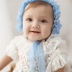 A stunning close-up of a baby girl with beautiful blue eyes, wearing a delicate lace bonnet. Her direct gaze is captivating.
