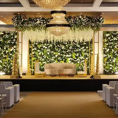 For this Vidhi ceremony, we designed a luxurious indoor stage featuring three massive green walls overflowing with white flowers. The look was completed with cascading wisteria from the ceiling and a grand chandelier, blending nature with opulence.