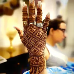 This intricate back-of-hand design features a detailed jaali or net pattern, with each finger covered in unique artwork. It's a classic choice for brides and wedding guests.