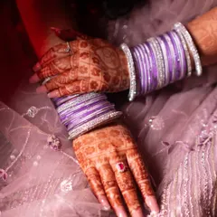 A detailed shot of the bride's hands, showcasing her beautiful mehndi, purple bangles, and engagement ring. The colors and textures tell a story of celebration.