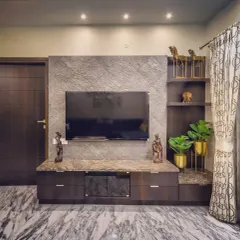 This custom TV unit combines a textured stone veneer backdrop with a polished Italian marble countertop. The dark wood drawers and open shelves provide ample storage and display space, while brass planters add a touch of metallic warmth.