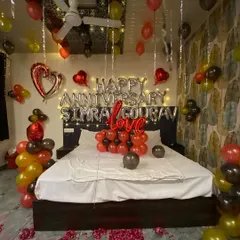 This is the full room view of the anniversary setup for Simran and Gourav. The decoration includes balloons on the ceiling, a custom message, and a floor covered in rose petals for a grand romantic gesture.