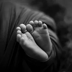 A close-up of a newborn's tiny feet, captured in black and white to highlight the wrinkles and details.
