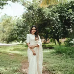 A full-length portrait showcasing the grace of a traditional Onam look. The serene, natural background allows the classic beauty of the Kerala saree to stand out.