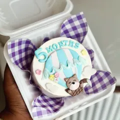 This five month bento cake is ready for an adventure, featuring a hot air balloon and a cute teddy bear. It's a small cake that tells a big story.