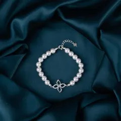 A modern silver and pearl bracelet with a four-leaf clover charm, beautifully styled on rich, dark fabric.