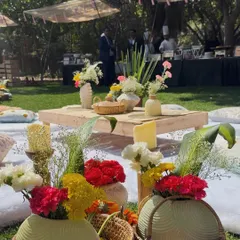 A close up of the vibrant tablescape for an outdoor picnic. We used colorful flowers in rustic baskets and vases, creating a cheerful and abundant centerpiece for the low picnic table.
