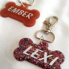 These custom pet tags for 'Ember' and 'Lexi' show off different styles. One is a solid color, while the other is full of fun, multi-colored glitter.