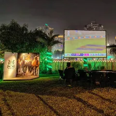 We host outdoor sports screenings on a giant projector, creating a mini-stadium feel. Here, guests enjoy a live cricket match on our lawn, a perfect setup for a community sports night.