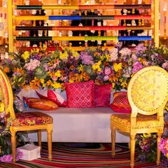 The main seating for the Mehendi, framed by a cascade of multi-colored flowers and a unique backdrop of colorful bangles. This design combines traditional elements with a modern, artistic flair.