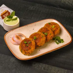 A platter of perfectly browned galouti or shami kebabs, garnished with cilantro and served with mint chutney and onion rings.