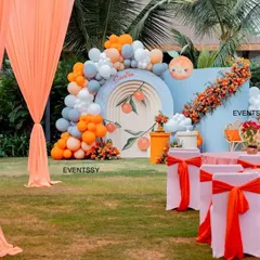 This wide shot shows the full outdoor setup for the orange-themed baby shower, including the draped tent entrance and guest seating arrangements. I ensure the entire event space feels cohesive and beautifully decorated.