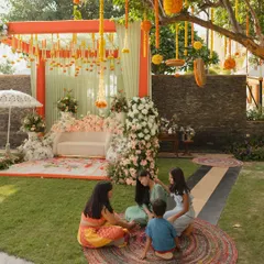 A relaxed moment at a daytime Mehendi, showing the guest seating area with colorful jute rugs and a stage decorated with pastel florals and mint green drapes.