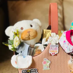 A closer view of the mom-to-be basket, showing the soft teddy bear, baby clothes, and the "Expecting a Little Pumpkin" sticker.