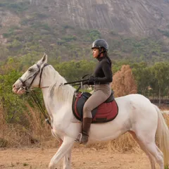 A rider confidently guides her white horse along a scenic trail with a stunning mountain backdrop, a typical view on our horse safari adventures.
