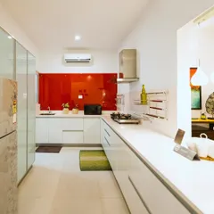 A bold, red lacquered glass backsplash adds a vibrant splash of color to this otherwise all-white modern kitchen. This accent feature creates a strong focal point and brings energy to the compact apartment space.