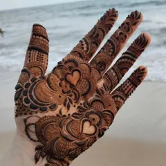 A bridal design with a hidden detail. This intricate hand henna, set against a beach backdrop, features small hearts within the pattern, adding a touch of romance.